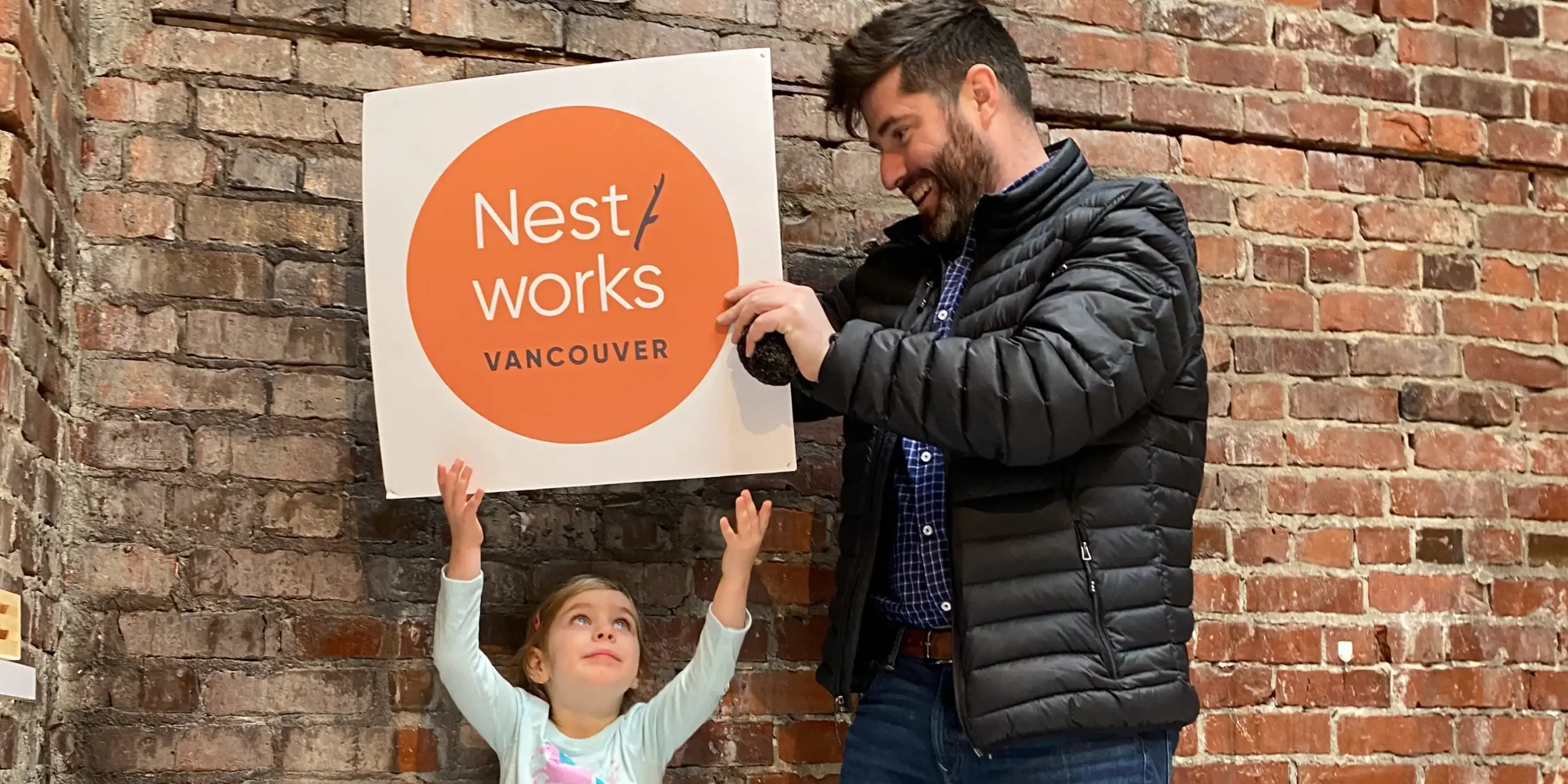 Dad and daughter holding NestWorks sign against interior brick wall