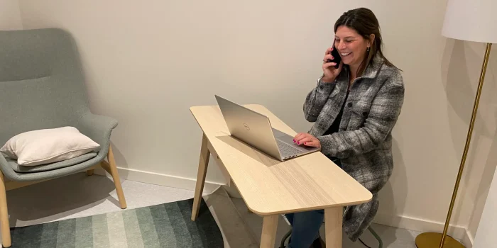 White woman sitting at desk with laptop laughing into a phone
